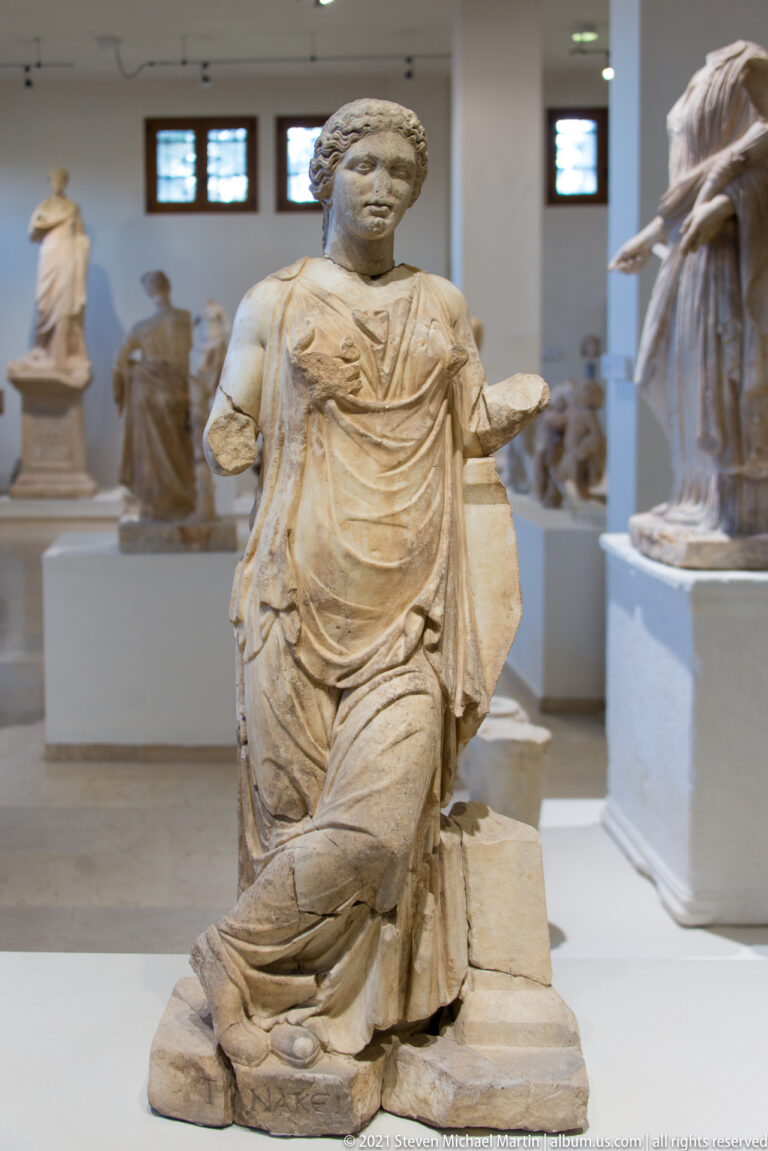 Seated marble female figure in layered drapery with both forearms incomplete and the head preserved.