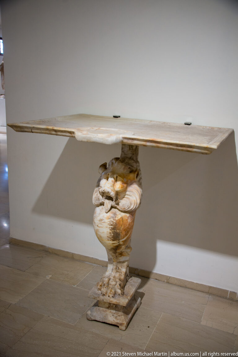 Rectangular stone slab supported by a short carved figural pedestal on a square base.