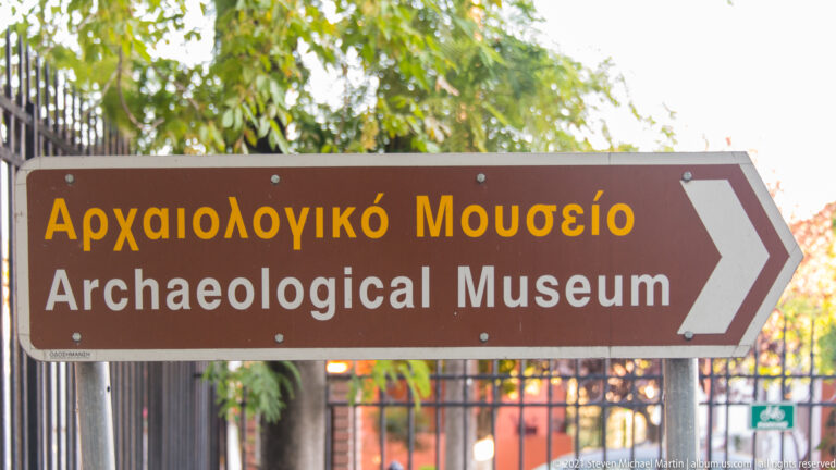 Brown bilingual Archaeological Museum sign with Greek and English text and a large arrow pointing right.