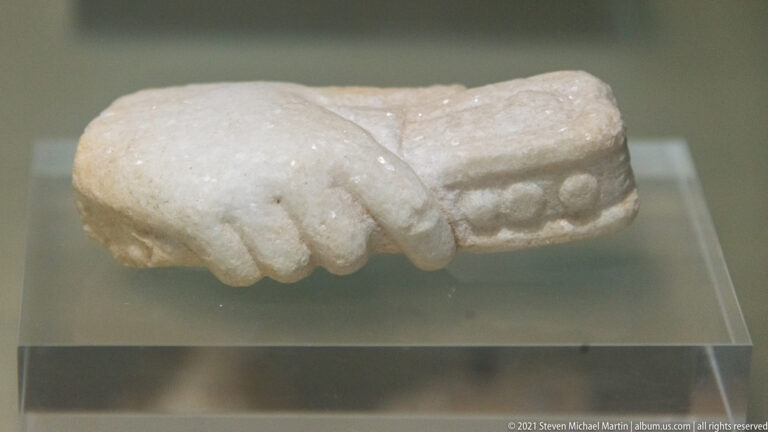 Detached marble hand gripping a short rectangular object with several raised circular details on its visible face.