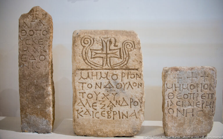 Three upright Greek-inscribed stone markers, two bearing clearly carved crosses, displayed together in the museum.