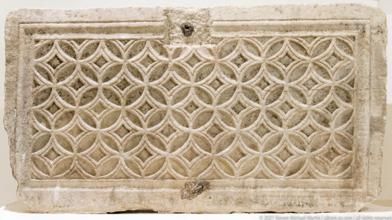 Rectangular stone panel with a molded border and dense repeating interlace of linked circular and leaf-shaped motifs.