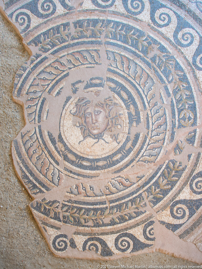 Closer view of a female-faced mosaic medallion surrounded by concentric ornamental bands and broken outer edges.