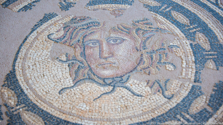 Close mosaic portrait of a woman with large eyes, center-parted hair, and curling locks inside a circular medallion.