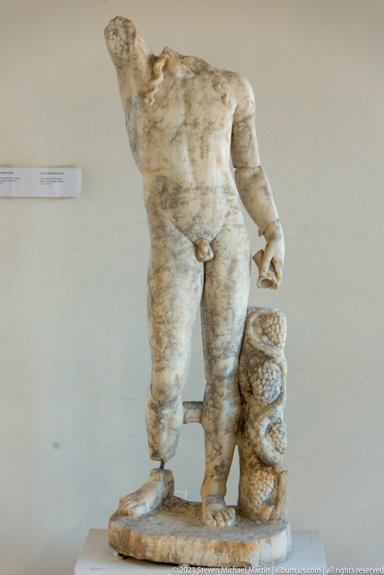 Headless marble male nude standing beside a thick coiled serpent used as a support.