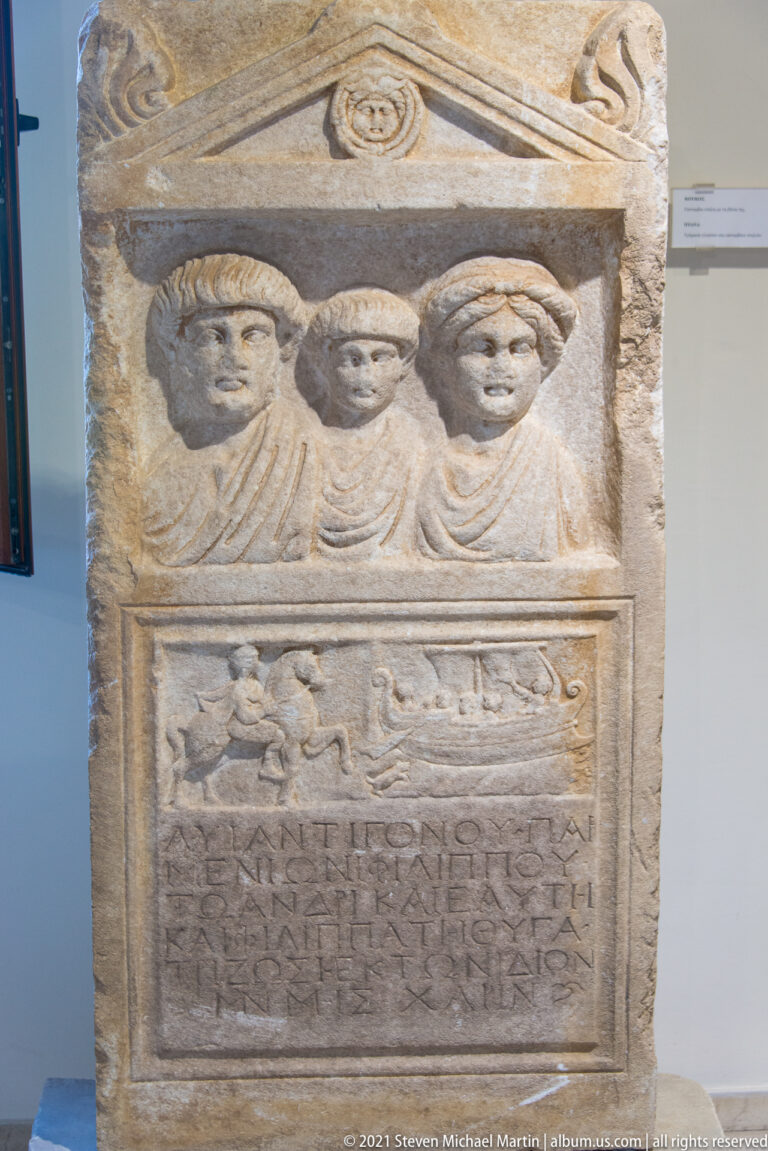 Stone stele with three busts beneath a pediment and a large Greek inscription panel below.