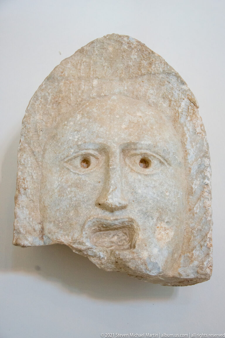 Semicircular pale stone fragment carved with a simple frontal human face and shallow facial features.