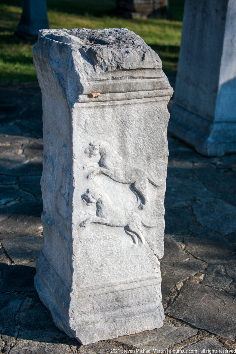 Weathered rectangular stone pedestal with molded edges and several dark metal fittings projecting from its front face.