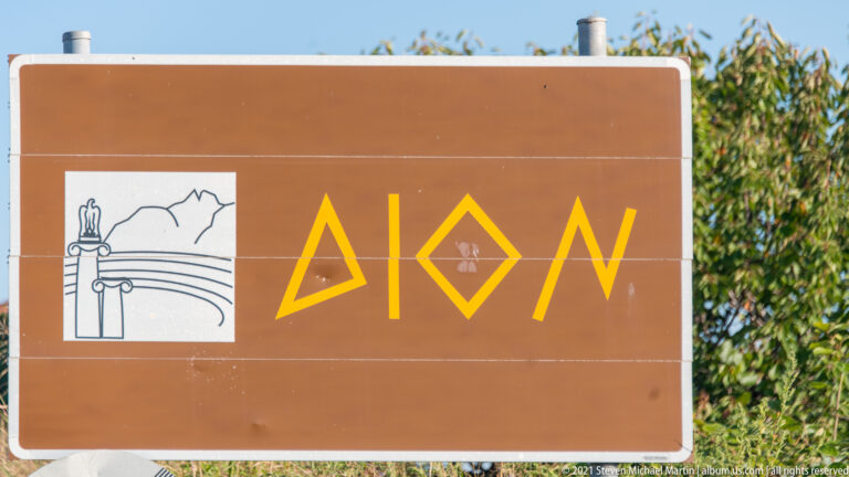 Brown entrance sign for the Archaeological Park of Dion with stylized Greek lettering and an architectural pictogram.