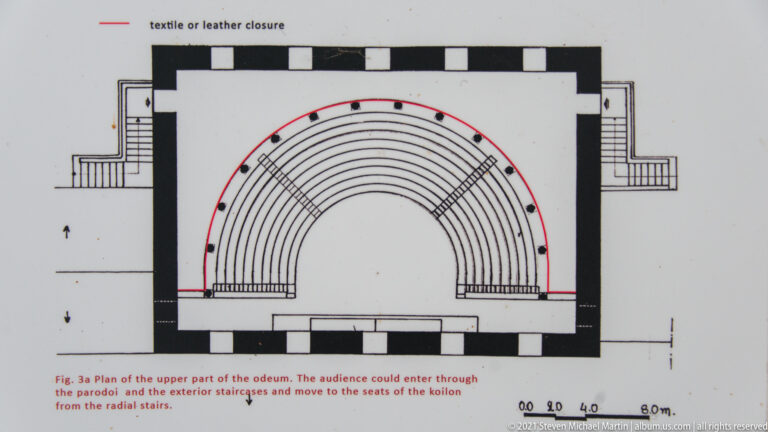Architectural plan of an odeum showing semicircular seating, perimeter walls, side passages, and red circulation markings.