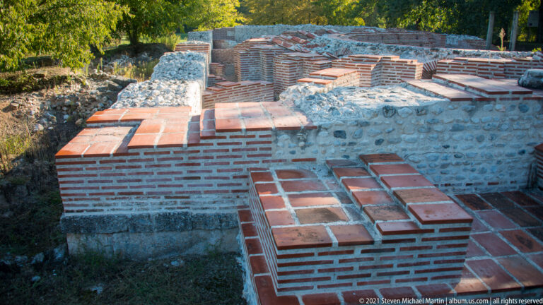 Low Roman bath walls of brick and stone with modern protective tile capping across several rectangular compartments.