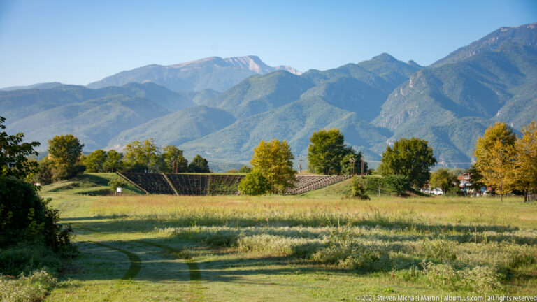 Archaeological landscape of Dion with Mount Olympus rising in the distance beneath a cloudy sky.