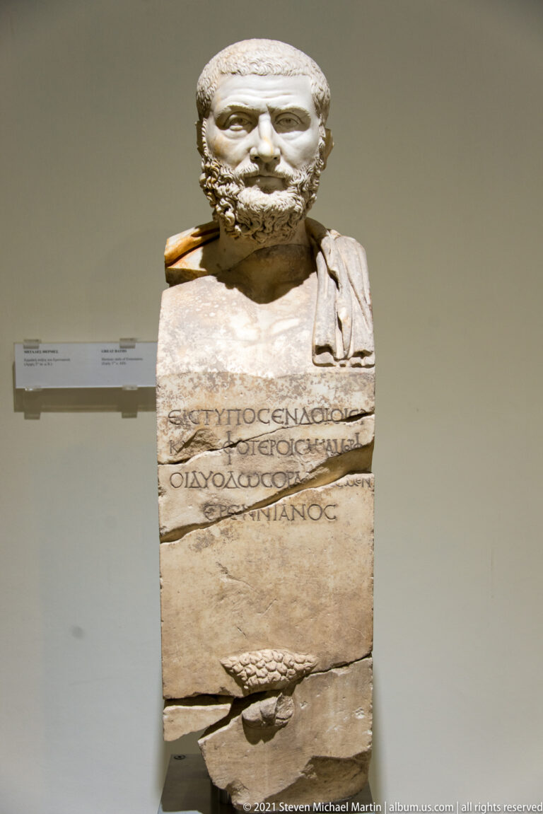 Bearded marble male portrait mounted on a rectangular inscribed pillar with Greek lettering and a projecting lower carving.