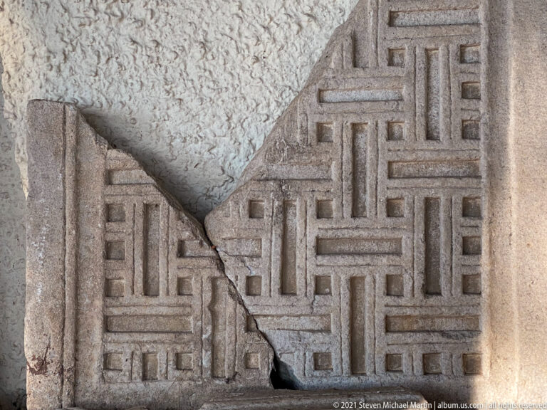 Broken stone panel carved with a dense interlocking meander pattern and a plain raised border along one edge.