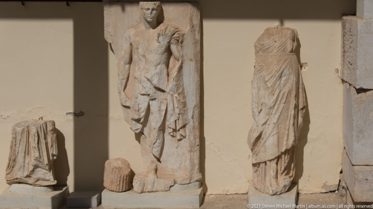 Several fragmentary ancient marble statues displayed against a museum wall, including standing draped figures.