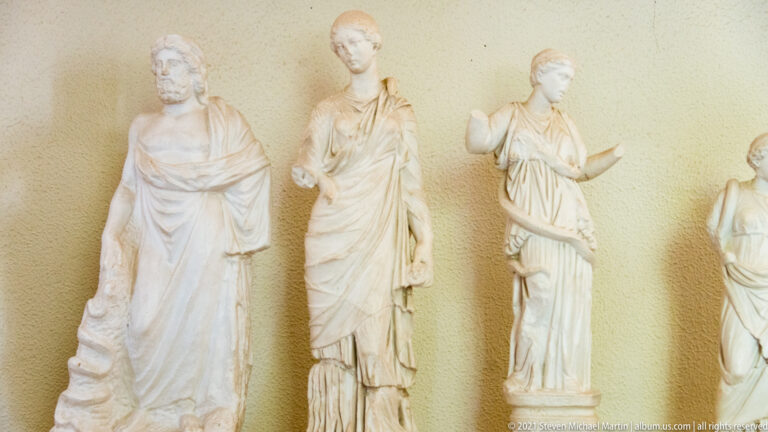 Three draped female marble statuettes standing side by side against a museum wall.