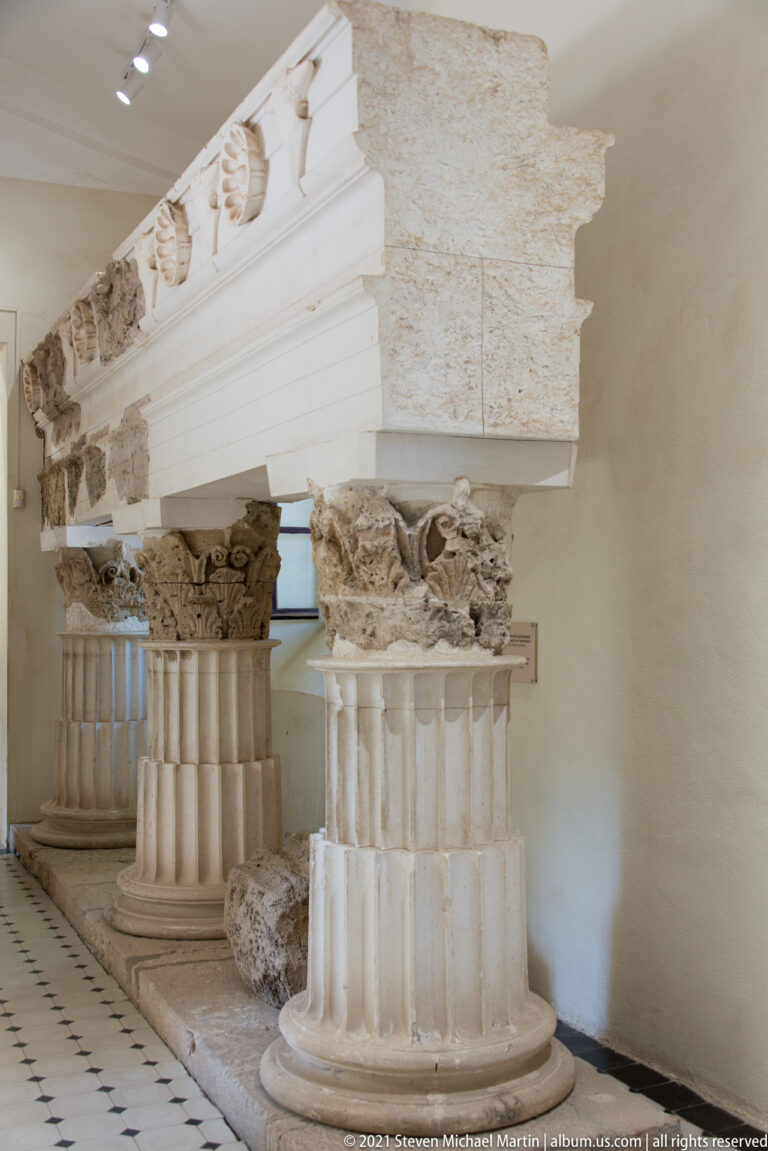 Reconstructed architectural display with fluted column drums, carved Corinthian capitals, and entablature fragments in a museum gallery.