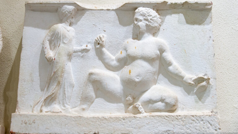 Marble relief with a nude seated male figure extending one arm beside a fragmentary draped standing figure.
