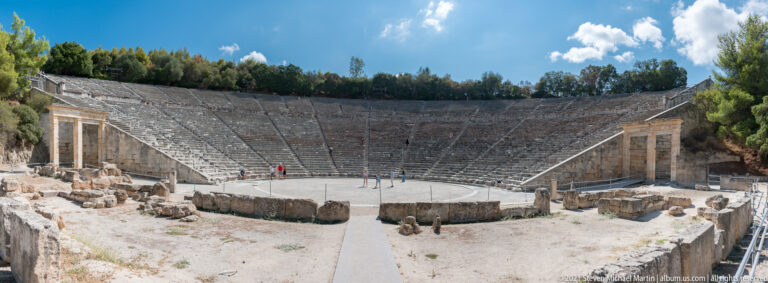 Centered frontal view of the orchestra and steep cavea, framed by masonry at the theatre’s two side entrances.