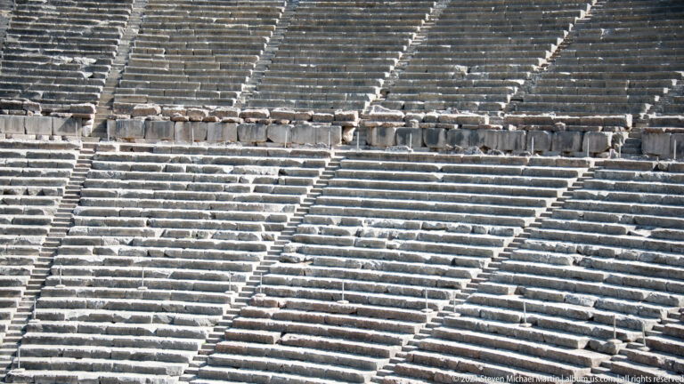 Telephoto view of dense horizontal stone seat rows crossed by steep radial stairways and a broad central passage.