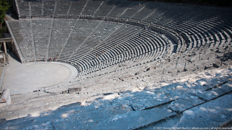 High oblique view over rough upper benches to the circular orchestra and tightly curved seating rows below.