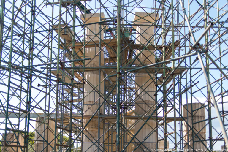 Dense steel scaffolding surrounding pale reconstructed architectural elements of the Tholos under conservation at Epidaurus.