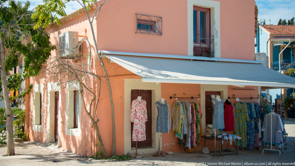 Dresses hang from racks beneath an awning outside a peach-painted two-story building with shuttered windows.