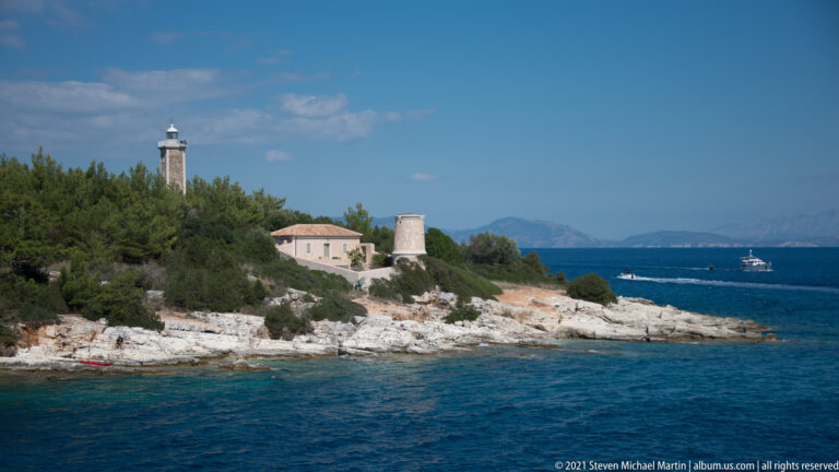 Lighthouse tower, keeper’s building, and shorter round masonry structure on a wooded rocky headland.