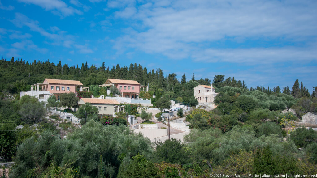Pale houses with tiled roofs scattered among olive trees and cypresses on a hillside above Fiskardo.