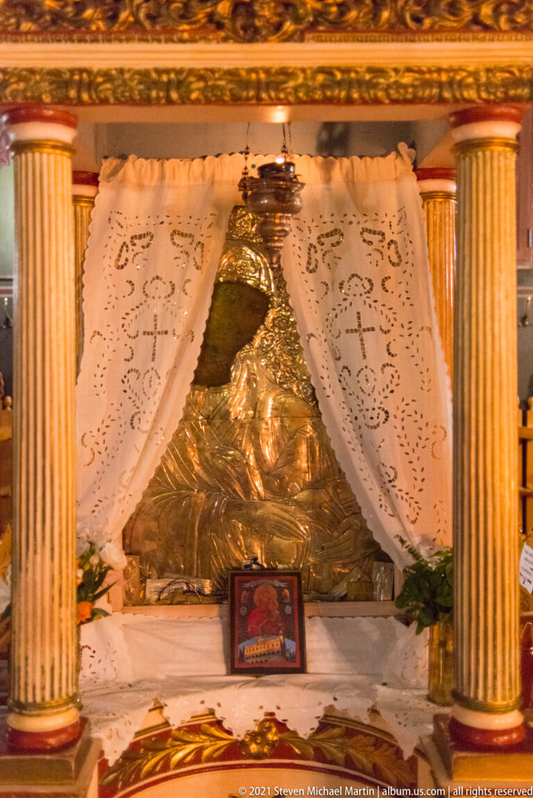 Silver-covered Orthodox devotional image behind embroidered white curtains and between gilded fluted columns.