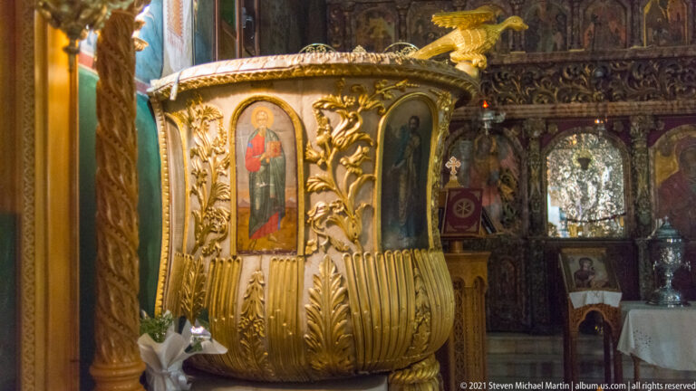 Gilded carved wooden Orthodox pulpit with painted saint panels and an eagle ornament, set before the iconostasis.