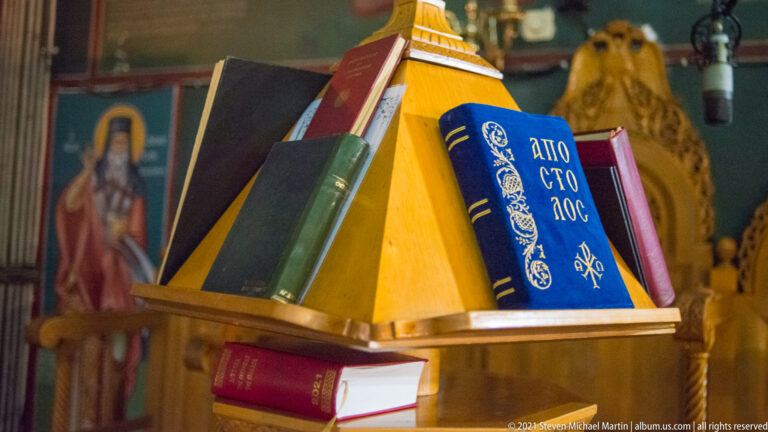 Greek Orthodox service books in blue, red, and green resting on a sloped wooden lectern.