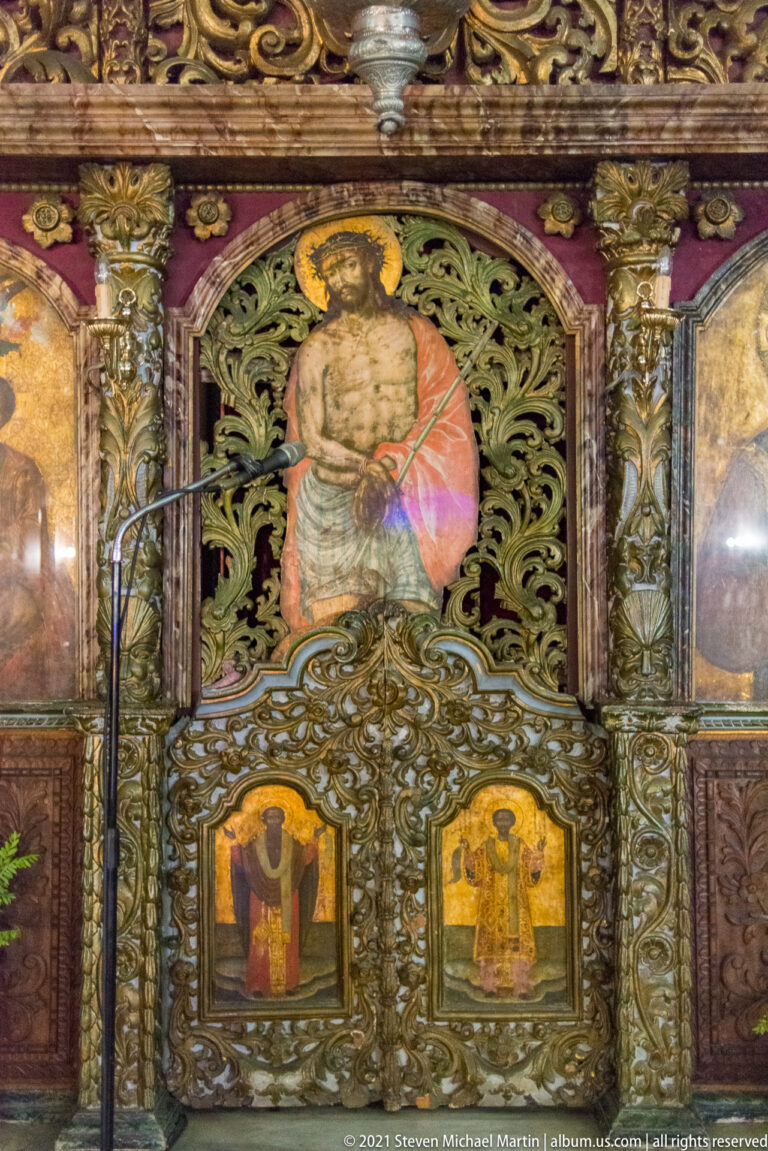 Close view of an Orthodox iconostasis with carved foliage, twisted columns, and three painted sacred images.