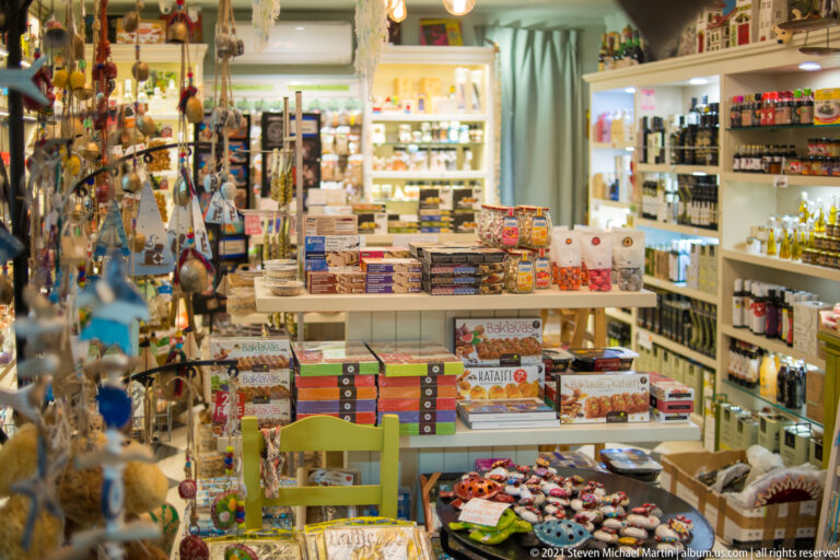 Packed souvenir shop with hanging trinkets, boxed goods, bottles, ornaments, and merchandise covering shelves and displays.