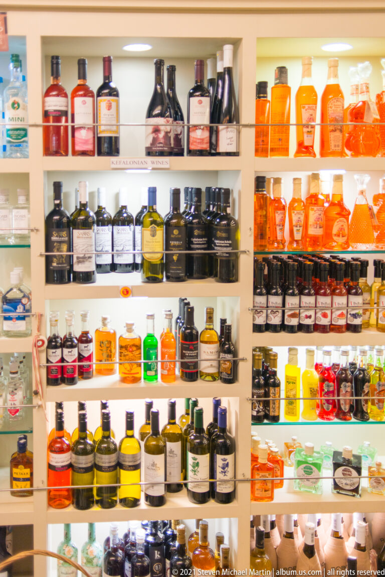 Bright white shelves filled with rows of dark, amber, green, red, and clear bottled spirits and liqueurs.