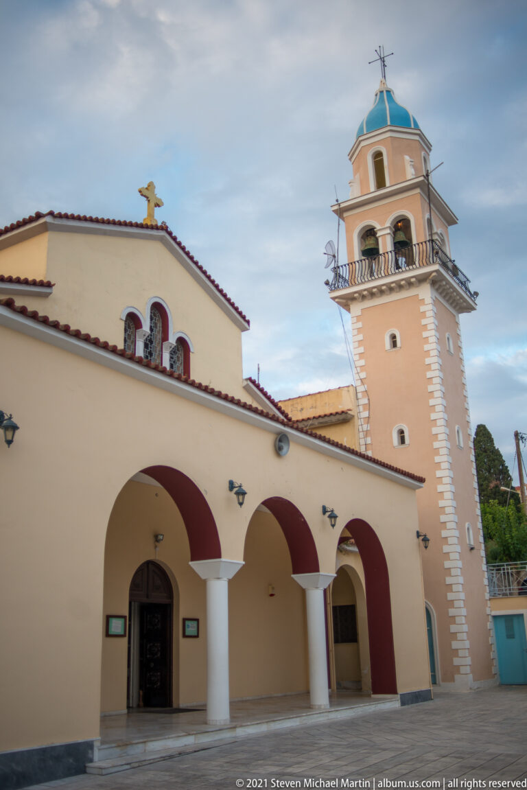 Orthodox church with three-arched porch, cross-topped roof, and tall bell tower capped by a blue polygonal roof.