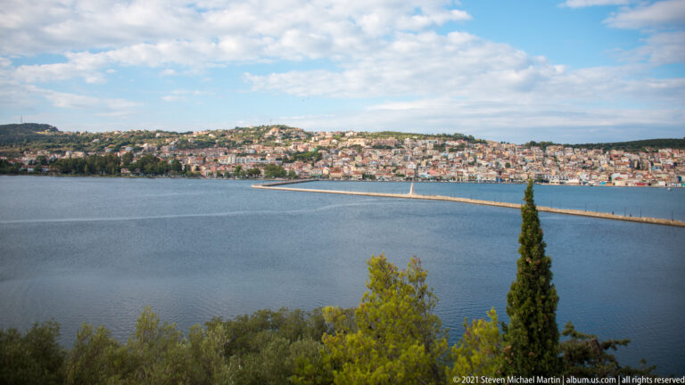 Wide bay with a long breakwater and densely built hillside town of pale houses and red roofs across the water.