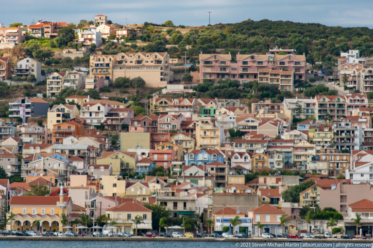 Dense hillside neighborhood of pastel houses and apartment buildings with red-tiled roofs above the waterfront.