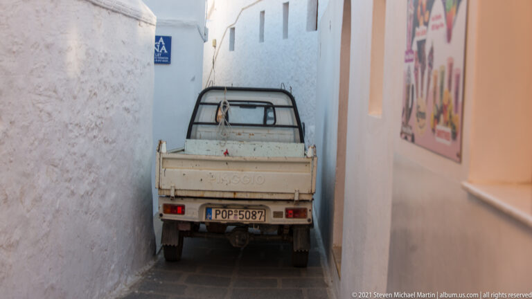 Small utility truck squeezed tightly between whitewashed walls in a narrow paved alley in Lindos.