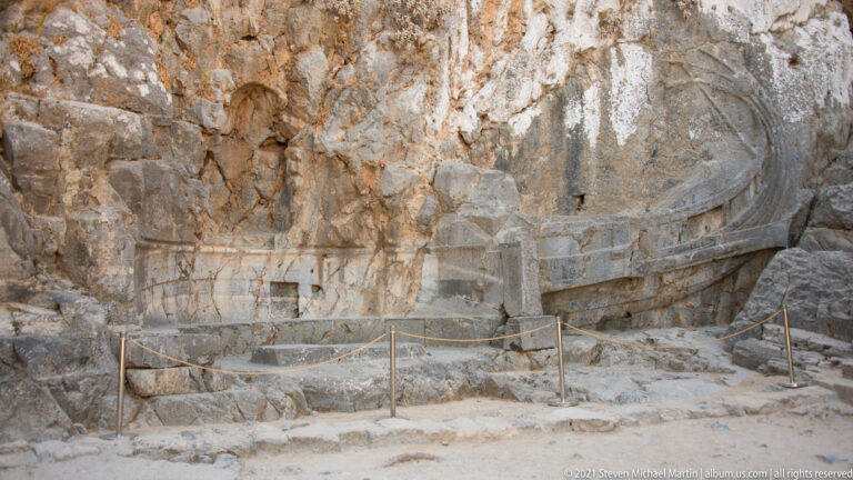 Rock-cut relief of a Rhodian trireme carved into the cliff beside rough stone steps at Lindos Acropolis.