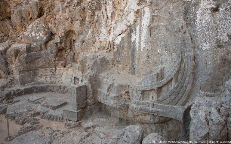 Oblique view of the rock-cut Rhodian trireme relief above stone steps and a protective rope barrier.