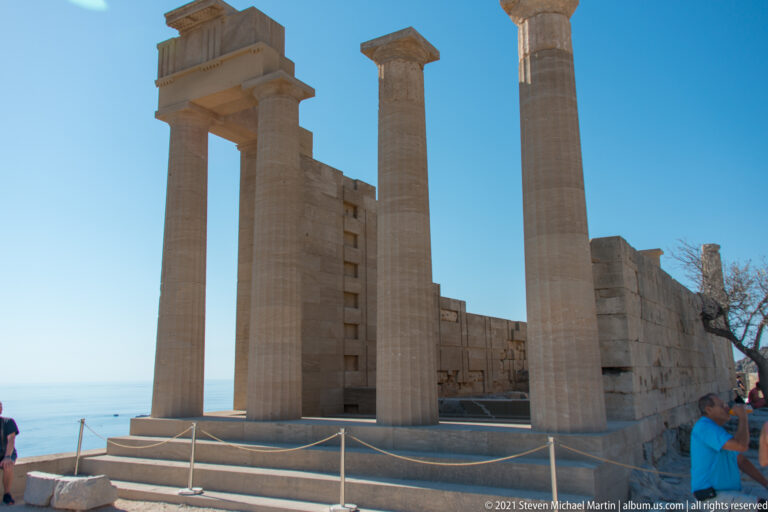 Tall restored columns, squared capitals and wall sections rise above steps and rope barriers on the sanctuary terrace.