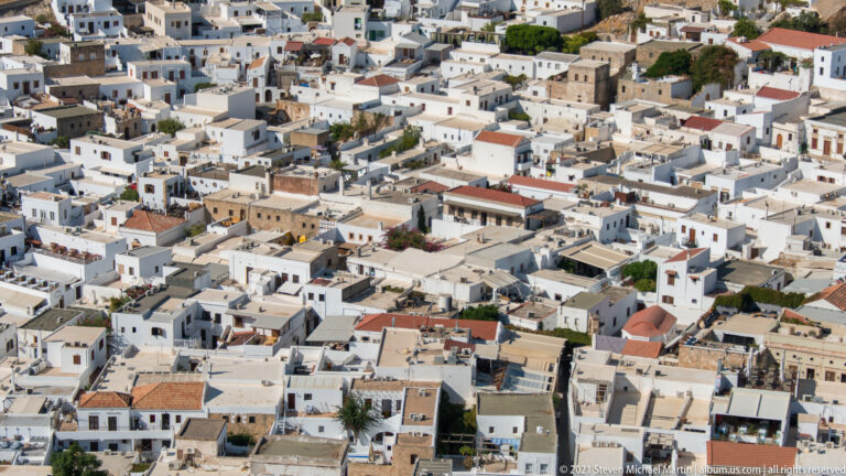 Dense cluster of whitewashed flat-roofed houses in Lindos village seen from the acropolis above.