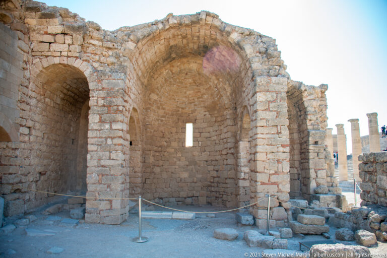 Two surviving vaulted bays with rough stone walls, brick-edged arches and a narrow window opening.