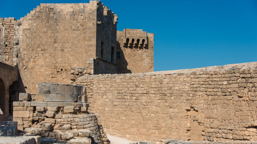 Massive stone walls and a projecting crenellated tower rise above lower fortifications at Lindos Acropolis.