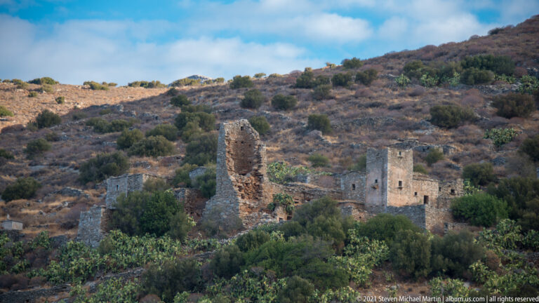 Roofless stone tower houses and ruined walls among shrubs on a dry hillside.