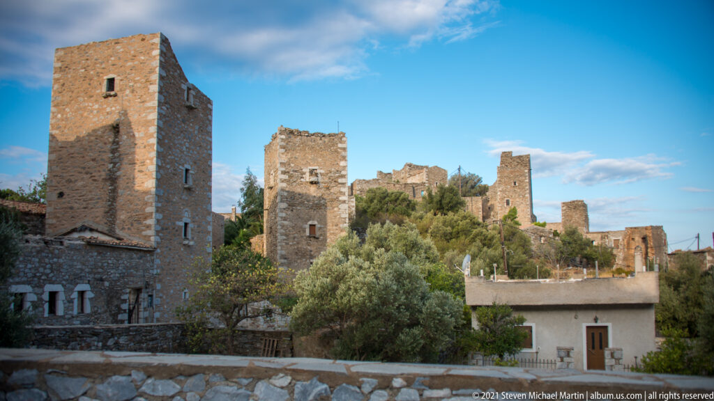 Several tall rectangular stone towers rising above trees and lower buildings beneath a blue sky.