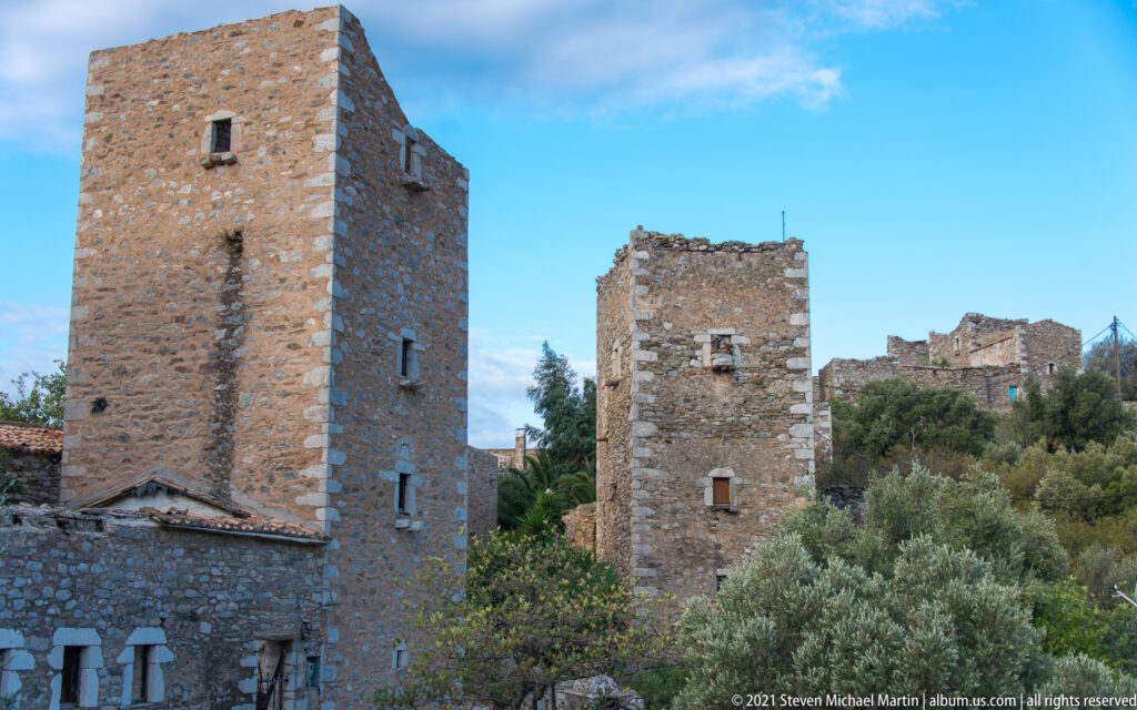 Two tall stone tower houses with small windows rising among trees and village buildings.