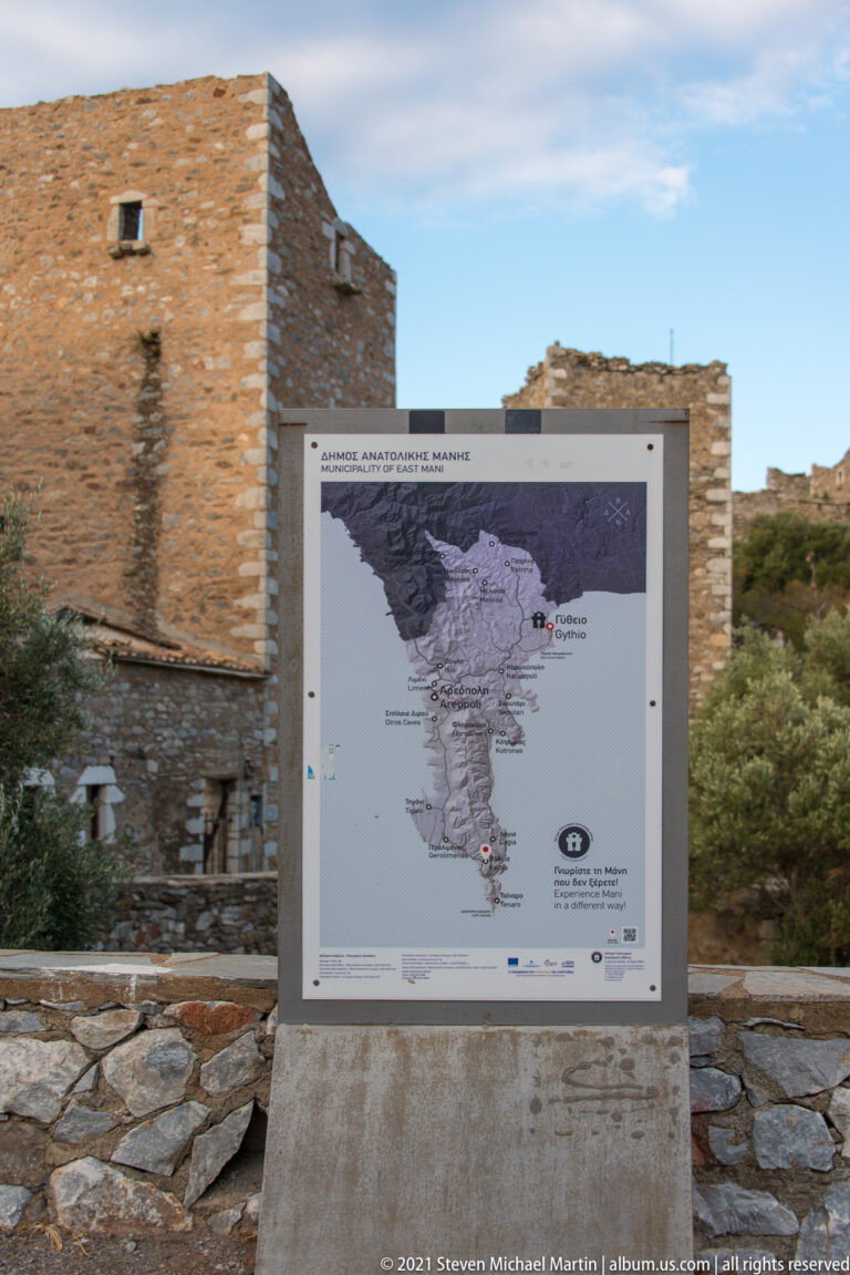 Mani Peninsula visitor map mounted on a stone base with historic stone towers behind.