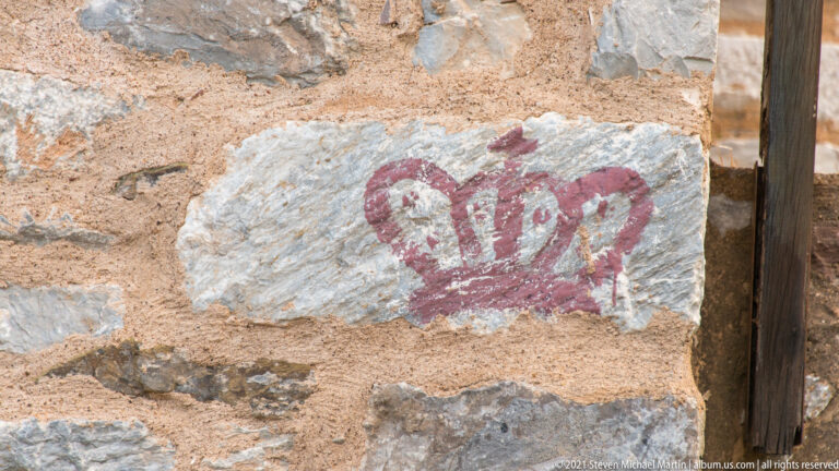 Red crown-shaped painted motif on a pale stone set into rough tan-and-gray masonry.